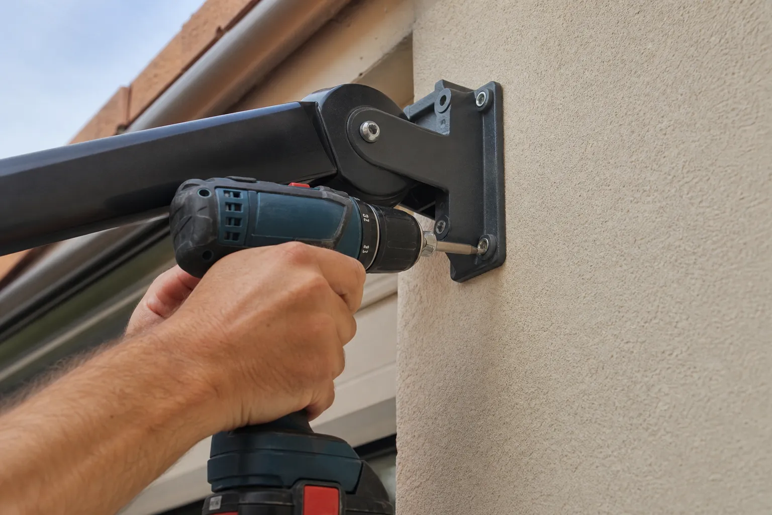 Mains d’un artisan fixant un bras de store banne au mur à l’aide d’une perceuse, gros plan sans visage