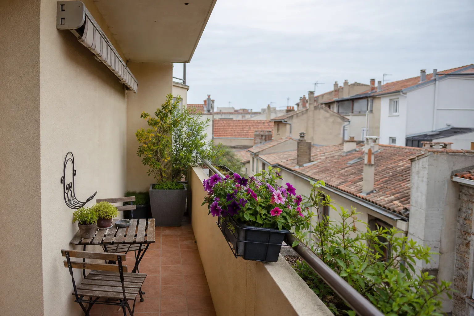 Balcon avec store banne replié et jardinières, toits de ville méditerranéenne en arrière-plan