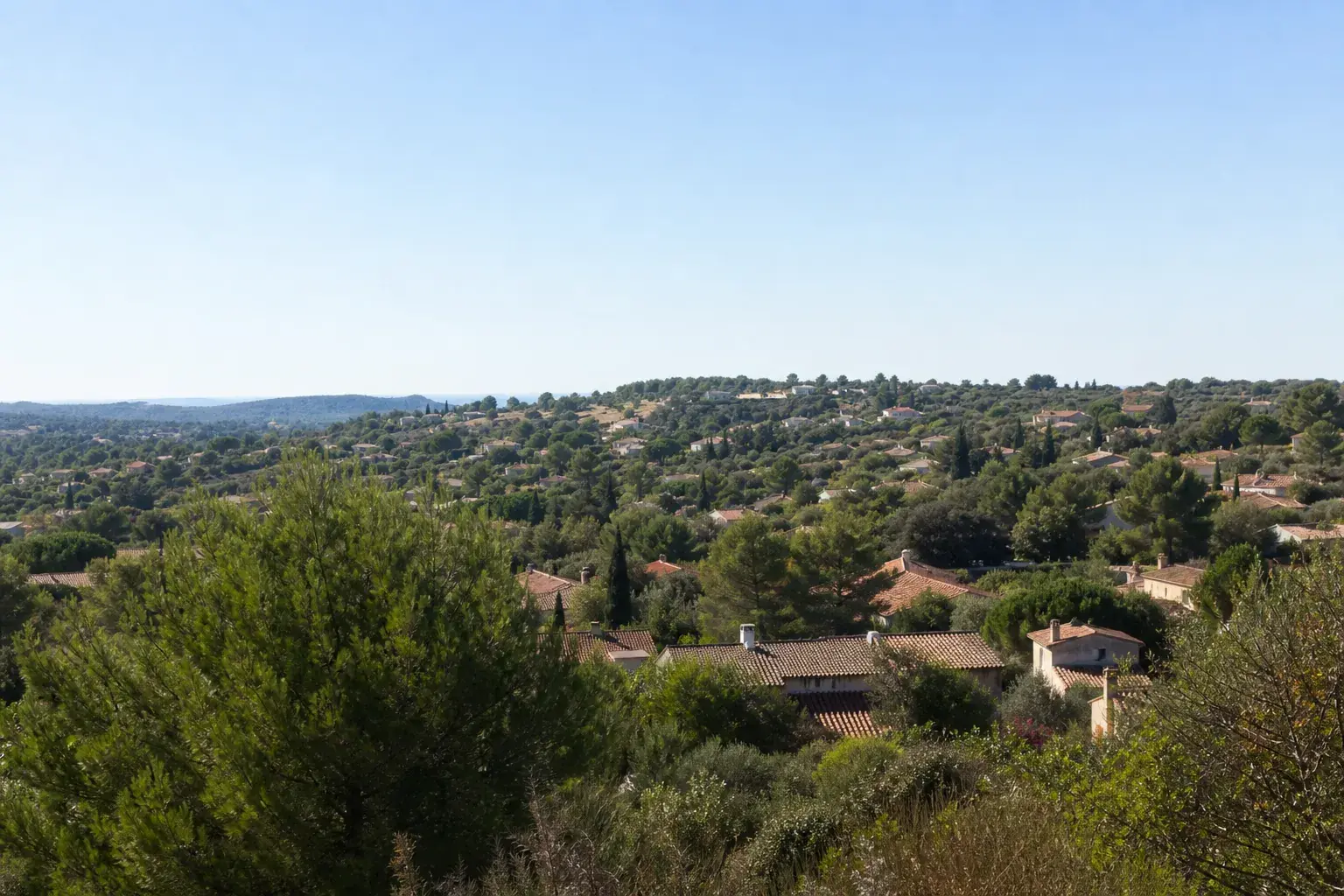 Vue large d’une colline provençale avec toits de tuiles et végétation méditerranéenne, ciel dégagé